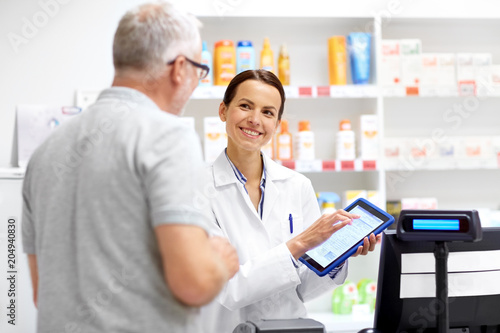 medicine, healthcare and technology concept - happy apothecary and senior male customer with digital prescription on tablet pc computer screen at pharmacy