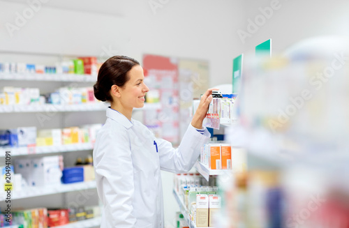 medicine, pharmaceutics, healthcare and people concept - happy female apothecary taking drug from shelf at pharmacy