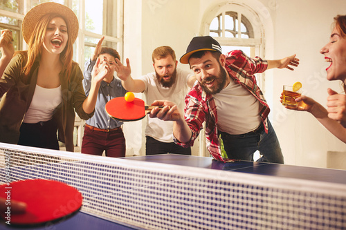 Group of happy young friends playing ping pong table tennis