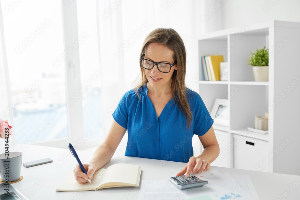 business, people, finance and accounting concept - happy woman with calculator counting and writing to notebook at office business, people, finance and accounting concept - happy woman with calculator counting and writing to notebook at office