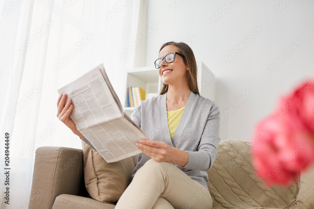 Obraz premium mass media and people concept - happy middle-aged woman reading newspaper at home