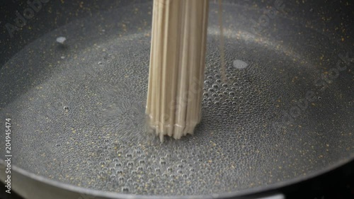 put Zaru Soba (Cold Soba Japanese Noodles food style) into boiled hot water air bubble and smokein black teflon induction pan and stir with wooden turner photo