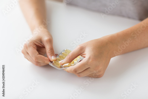 medicine, healthcare and people concept - woman hands opening pack of cod liver oil capsules
