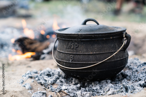 cast iron pot being used to cook a camping meal with coals and a wood burning camp fire
