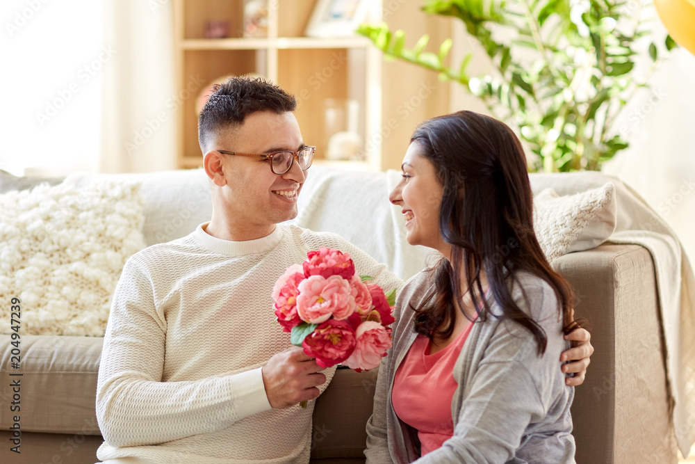 family, holidays and greetings concept - happy husband giving flowers to his wife at home family, holidays and greetings concept - happy husband giving flowers to his wife at home
