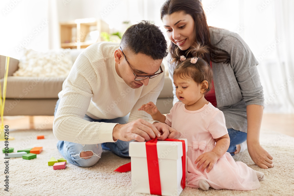 family, holidays and people concept - mother, father and happy little daughter with gift box at home birthday party family, holidays and people concept - mother, father and happy little daughter with gift box at home birthday party