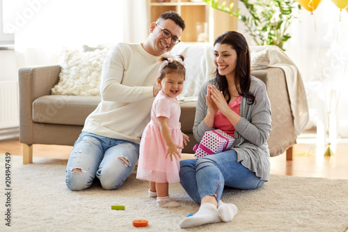 family, holidays and people concept - mother, father and happy little daughter with gift box at home birthday party