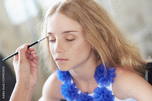 Stylist doing the make-up for a beautiful little girl model.