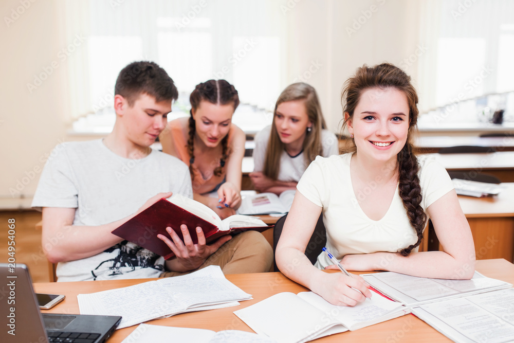 Concept students and teamwork. Three productive studying friends sitting in the library and learning together from notes and the books while one curly smiling girl from a group looking at the camera. Concept students and teamwork. Three productive studying friends sitting in the library and learning together from notes and the books while one curly smiling girl from a group looking at the camera.