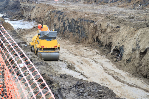 road roller compacts the sand in a deep trench.