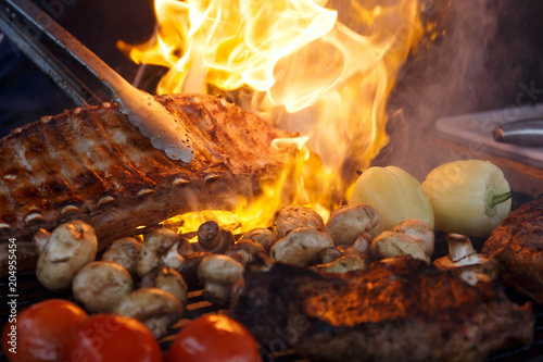 Meat  mushrooms and vegetables are fried on the grill in a barbecue with flames. Ribs  champignons  tomatoes and peppers are fried over an open fire. Appetizing meal on the bbq. Selective focus