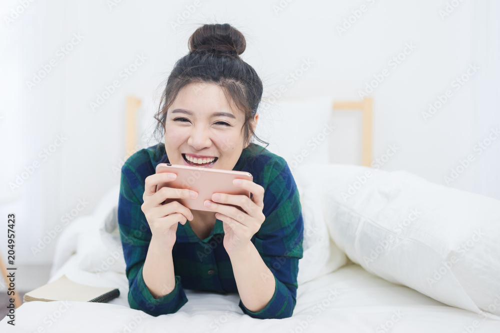 Portrait of beautiful Asian woman on bed while use smartphone with attractive smiling Portrait of beautiful Asian woman on bed while use smartphone with attractive smiling