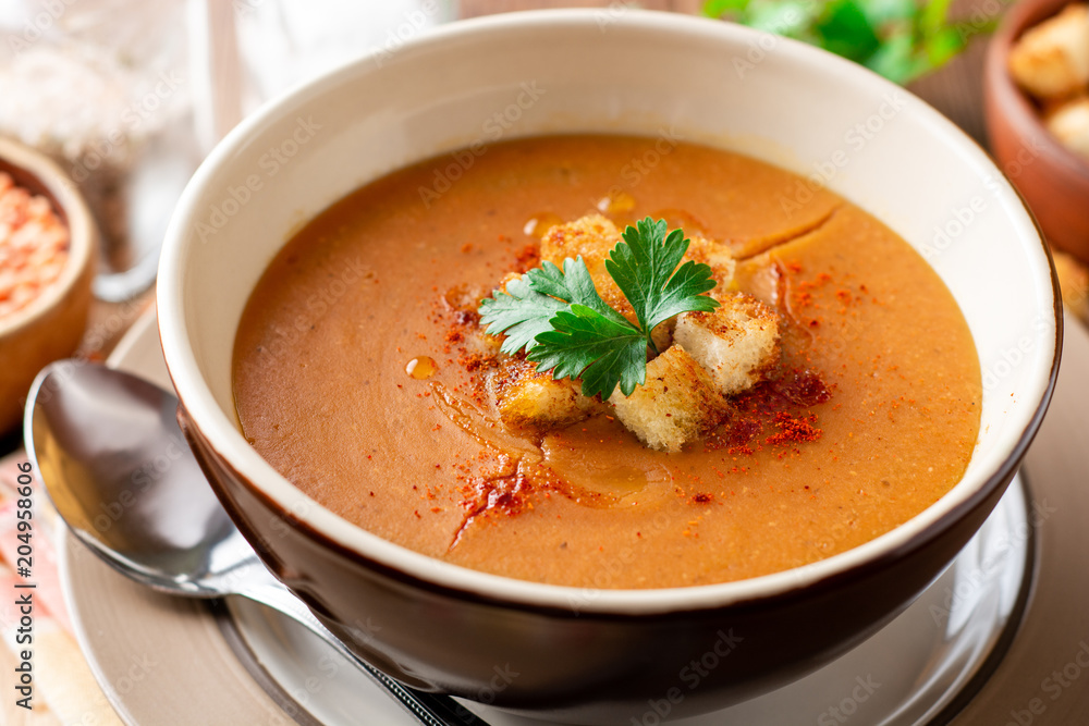 Red lentil cream soup with croutons in bowl on wooden table Red lentil cream soup with croutons in bowl on wooden table