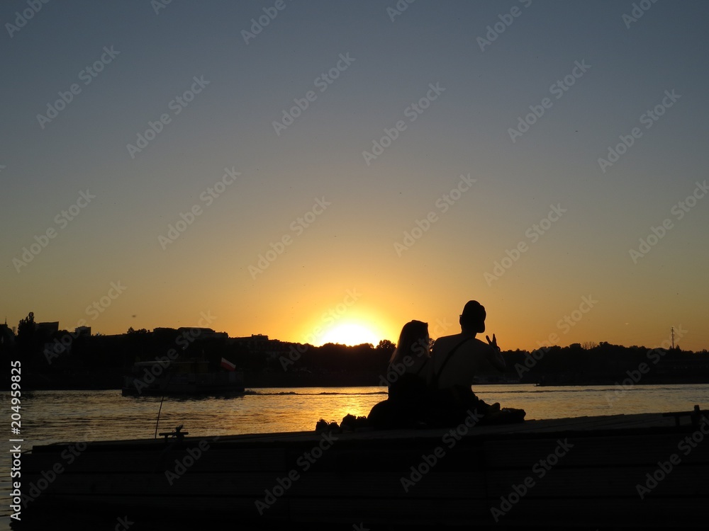 Happy Couple in Love Enjoying Romantic Scene of Sunset Sitting on Wharf at River