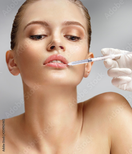 Beautiful woman face and beautician hands with syringe makes cosmetic injection in the upper lip. Clean Beauty concept
