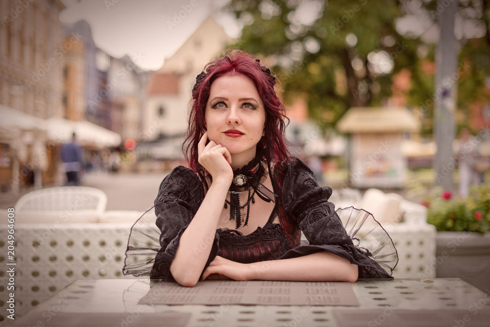 Young gorgeous redheaded woman sitting in an outdoor cafe dressed in retro fashion clothes.