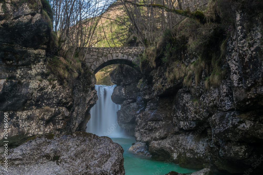 Cascata del rio Repepeit con il famoso antico ponte, vista di una valle alpina Cascata del rio Repepeit con il famoso antico ponte, vista di una valle alpina