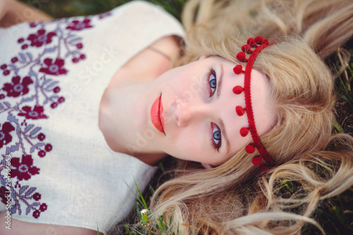 tender blonde woman lies on the grass dressed in a natural embroidered dress bandage on her head  on a green background stylish and cozy. The concept of love advertising is panoramic