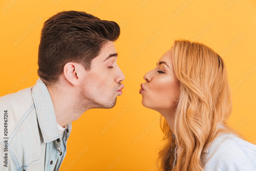 Profile photo of young beautiful people in love expressing love and affection while kissing each other with closed eyes, isolated over yellow background Profile photo of young beautiful people in love expressing love and affection while kissing each other with closed eyes, isolated over yellow background