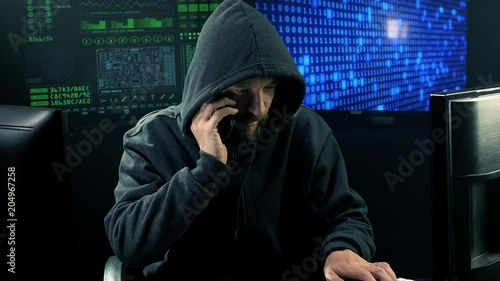 Man with hood in office tipying quick talking on the phone at night tracking shot photo