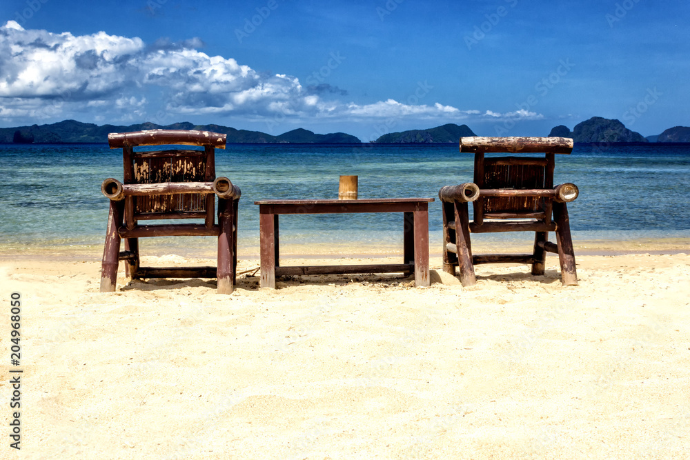 Fototapeta premium Table and chairs on an exotic beach on a hot sunny day against the blue sea and sky.