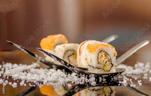 Close up of delicious sushi rolls over a metallic spoon with small grains of salt served on black table