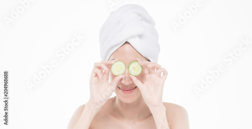 beautiful asia woman with towel on head with perfect clean skin smiling holding cucumber slices over white background. Beauty cosmetology and spa.