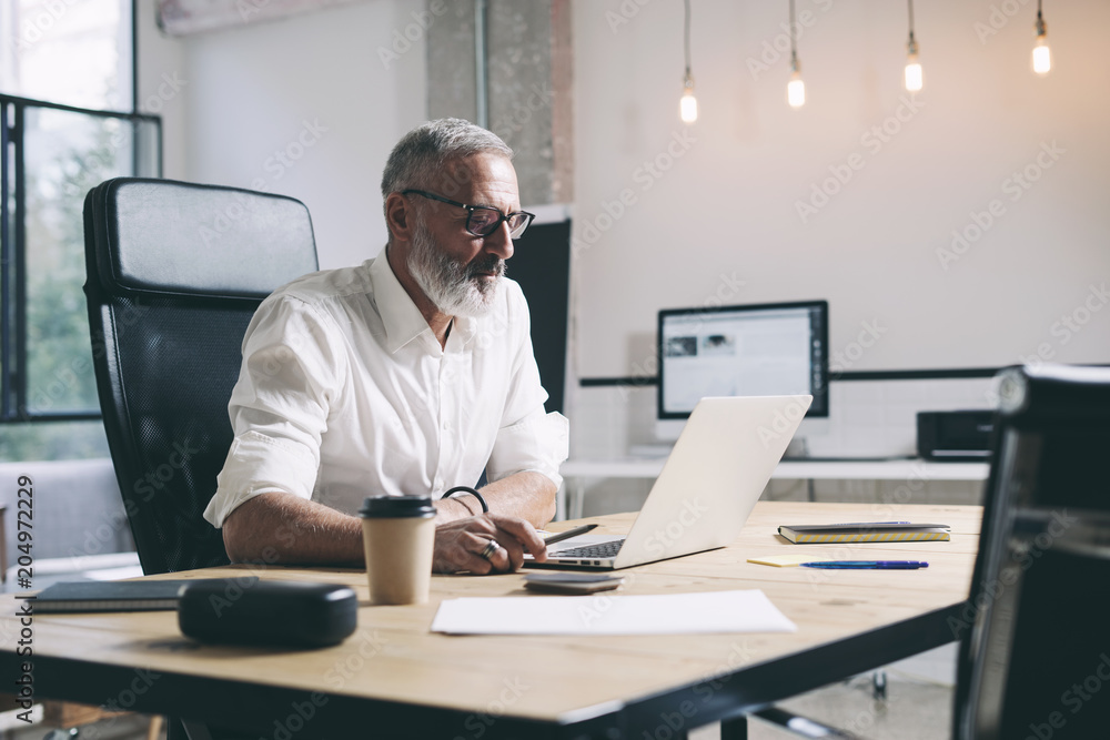 Middle age businessman working on mobile laptop computer while sitting at wooden table at modern office place. Middle age businessman working on mobile laptop computer while sitting at wooden table at modern office place.