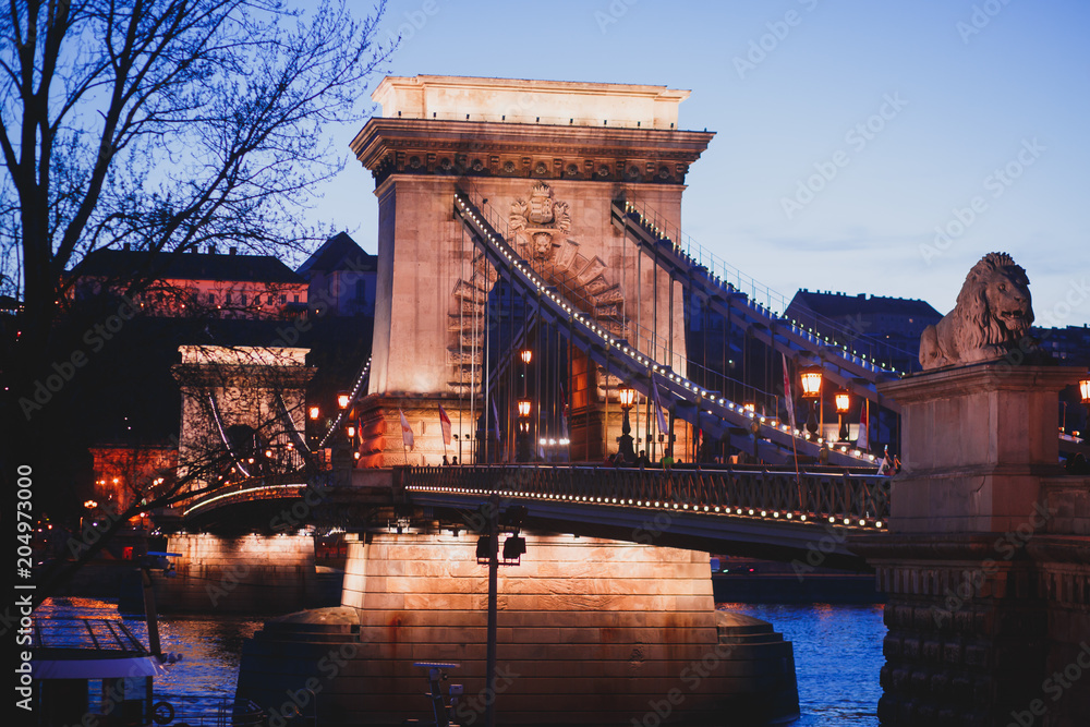 Obraz premium Night view of a famous Budapest Szechenyi Chain Bridge, a suspension bridge that spans the River Danube between Buda and Pest, the western and eastern sides of Budapest