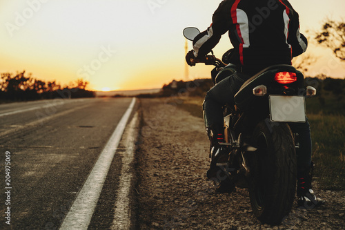 Back view crop of a motorcyclist traveler starting his road after resting against sunset. photo