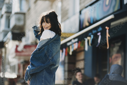 Portrait of a amazing young girl walking on the street and posing to the photographer smiling and touching her hair against a colorful coffee shop. © Strelciuc