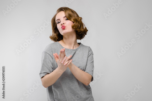 Charming young girl in a gray T-shirt on a gray background. The girl folded her fingers in the form of a pistol