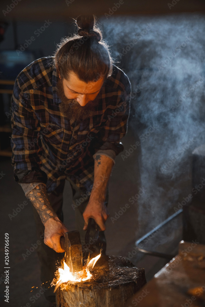 Blacksmith works as a hand hammer with molten metal on the anvil in the smithy with a spark firework. Blacksmith works as a hand hammer with molten metal on the anvil in the smithy with a spark firework.