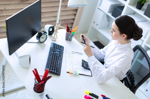 A young girl in the office sits at a table, holds a marker and a pencil in her hand and works with a computer, a calculator and documents.