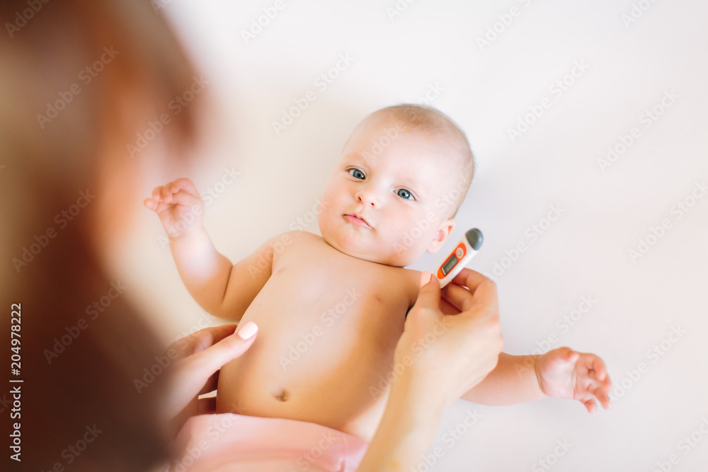 Mother holding thermometer of her ill baby.Sick baby on bed with fever measuring temperature Mother holding thermometer of her ill baby.Sick baby on bed with fever measuring temperature