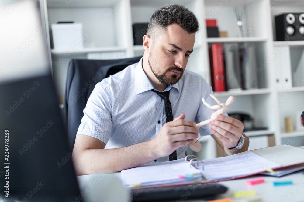 A man is sitting at a table in the office and is looking at a wooden man. A man is sitting at a table in the office and is looking at a wooden man.