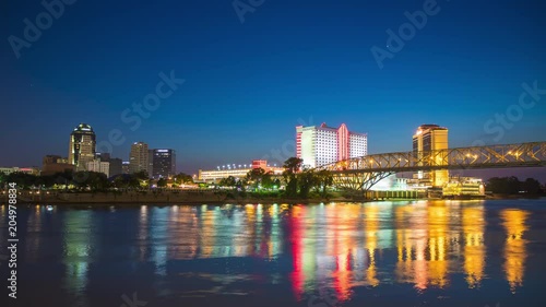 Shreveport LA Cityscape Night Timelapse with Lights from Skyscrapers and Casinos Reflecting onto the Moving Red River on a Blue Sky Background