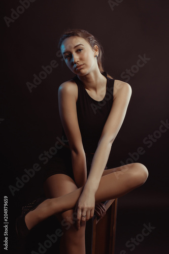 Studio photo session for a young lovely girl posing in the shadows, wearing black apparel