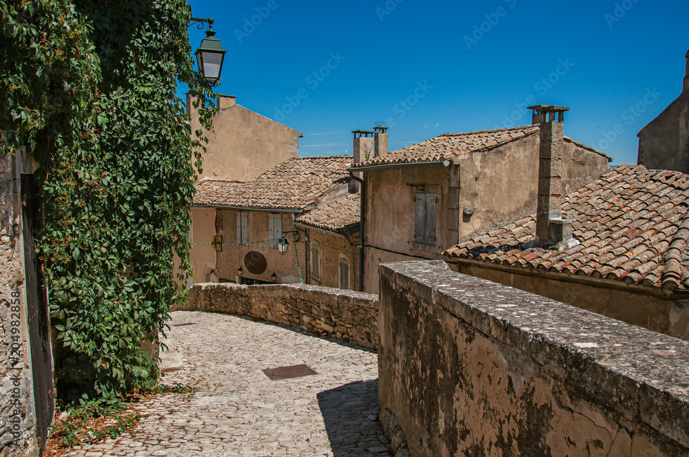 View of typical stone houses with sunny blue sky, in an alley of the historical village of Menerbes. Located in the Vaucluse department, Provence-Alpes-Côte d'Azur region, southeastern France