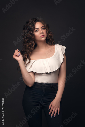 A brunette girl with a stylish hairstyle, professional make-up, clean skin posing in the studio on a dark isolated background. The model demonstrates its stylish outfit