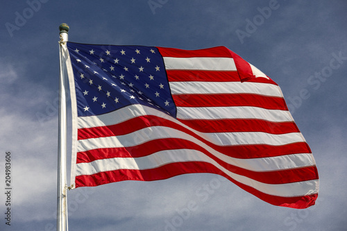 American flag waving in the wind with blue sky and white clouds in the background.