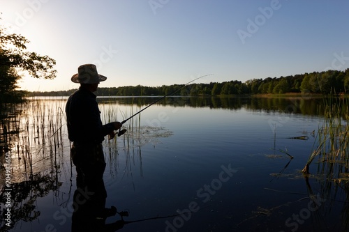 Silhouette of fisherman standing in the lake and catching the fish at sunny day