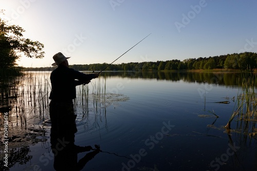 Silhouette of fisherman standing in the lake and catching the fish at sunny day © mtmmarek