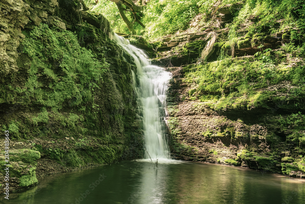 Beautiful mountain rainforest waterfall with fast flowing water and rocks, long exposure. Natural seasonal travel outdoor background in hipster vintage style