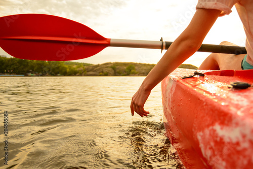 Young Woman Playing with Water while Sitting in Kayak on Beautiful River or Lake at Sunset. Close up of Female Hand.