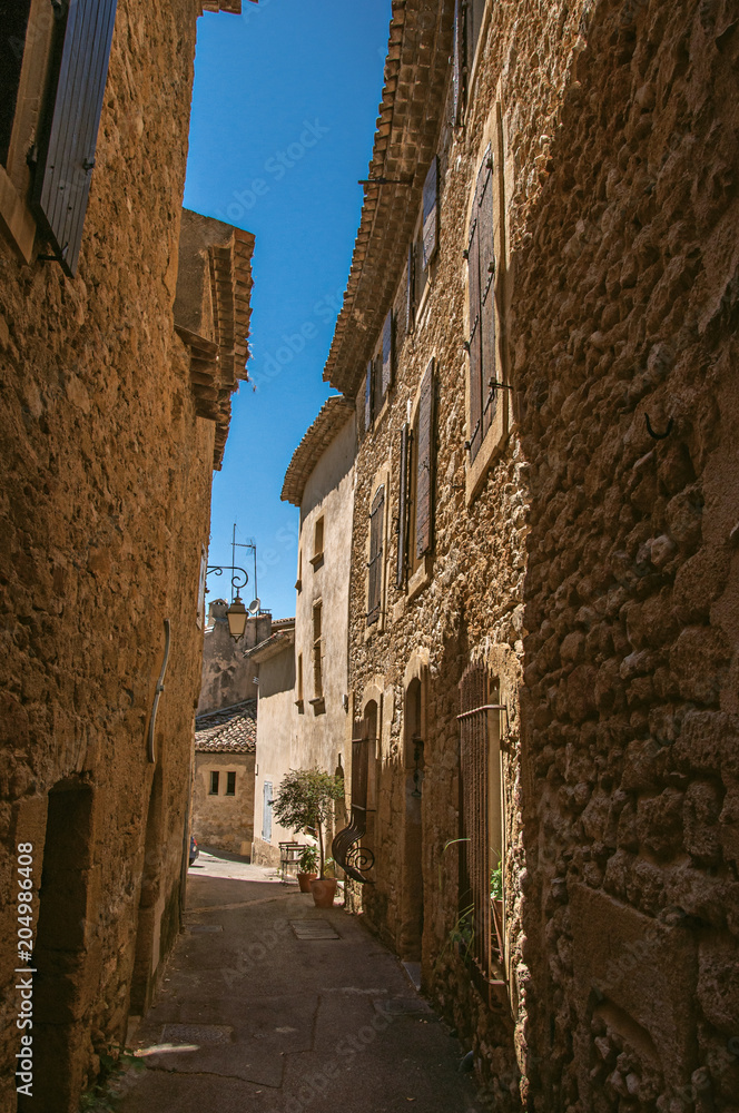 View of typical stone houses with sunny blue sky, in a narrow alley of the historical village of Lourmarin. In the Vaucluse department, Provence-Alpes-Côte d'Azur region, southeastern France