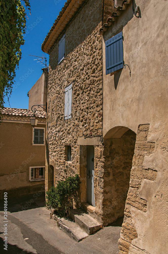 View of typical stone houses with sunny blue sky, in a raised alley of the historical village of Lourmarin. In the Vaucluse department, Provence-Alpes-Côte d'Azur region, southeastern France
