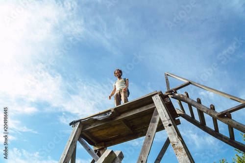 Junger Mann steht lachend auf einem Hochsitz vor blauem Himmel