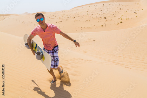 Young guy sand boarding down the dunes in the desert near Abu Dhabi.