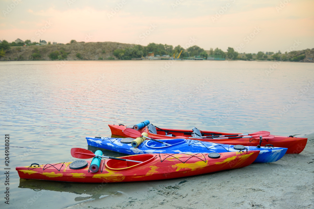 Three Traveling Kayaks on the Sand Beach near Beautiful River or Lake at the Evening. Travel and Adventure Concept. Three Traveling Kayaks on the Sand Beach near Beautiful River or Lake at the Evening. Travel and Adventure Concept.